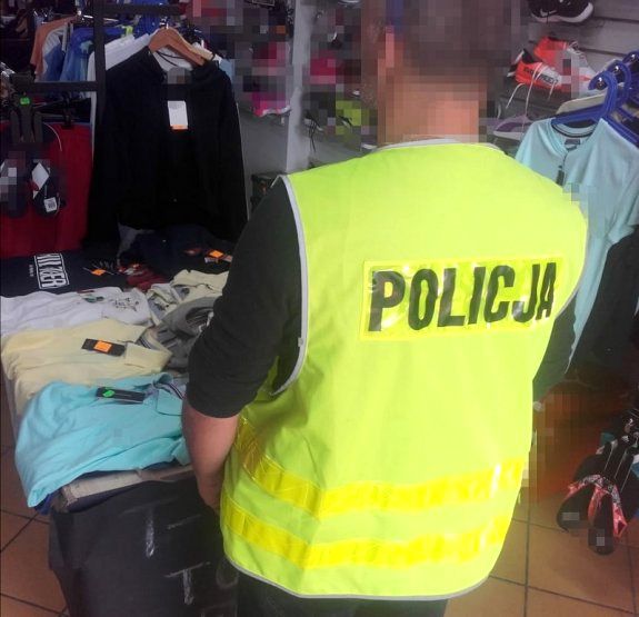 policjant stoi przy zabezpieczonych podróbkach odzieży